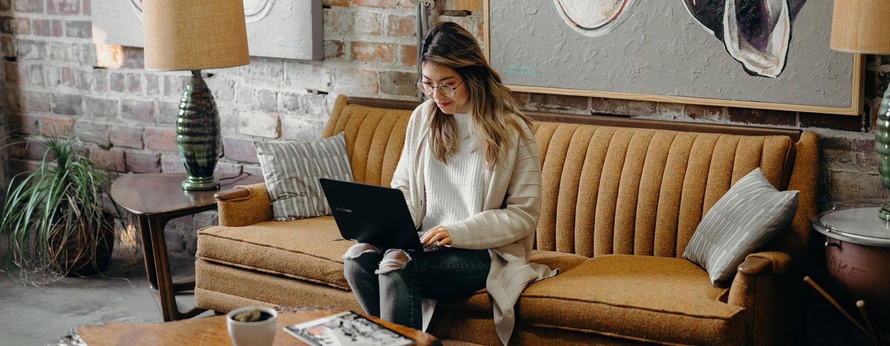 a woman sitting on a couch working on a laptop